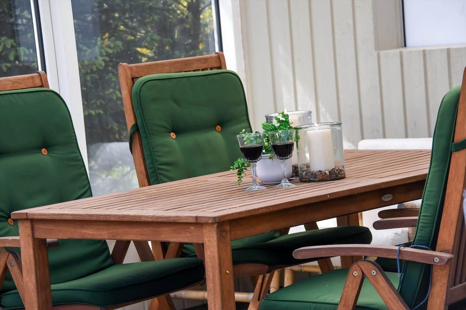 Holztisch mit grünen Sitzkissen und zwei Weingläsern auf einer Terrasse.
