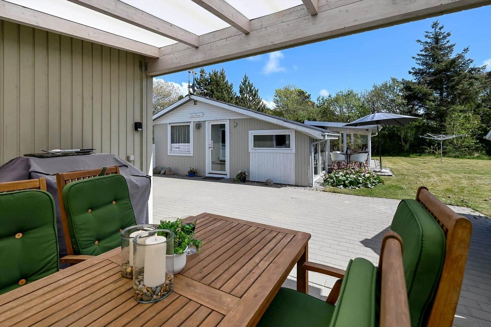 Terrasse mit Holztisch und grünen Sitzkissen. Im Hintergrund das Haus und Garten.