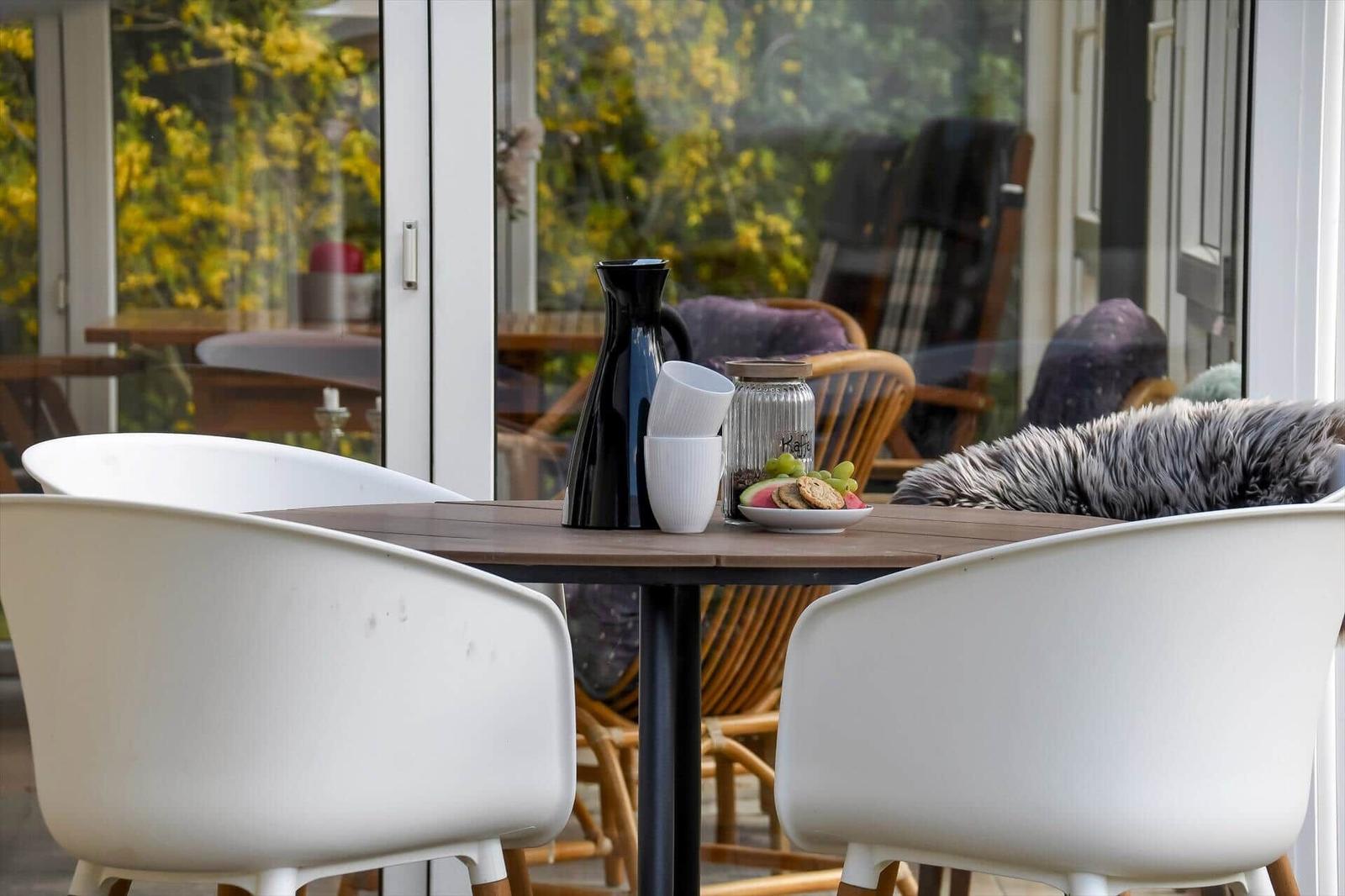 Ein Tisch mit Stühlen und Früchten vor einem Fenster mit Blick auf den Garten.