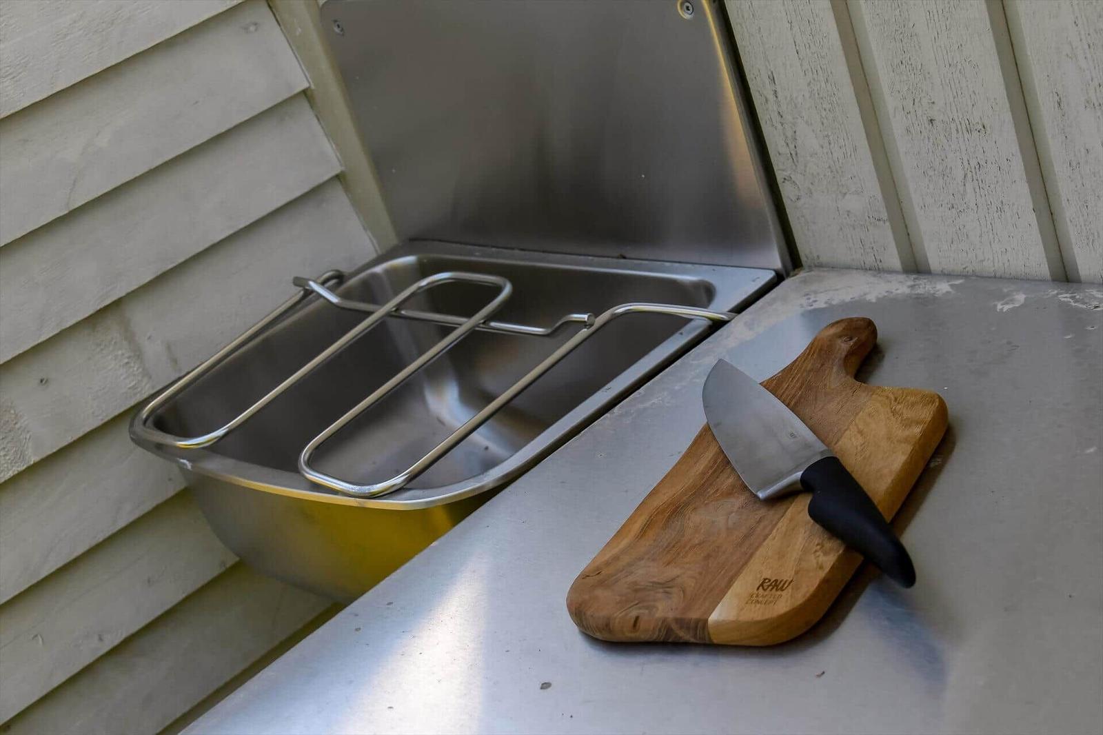 Außenküche mit Edelstahlwaschbecken und Holzbrett mit Messer.