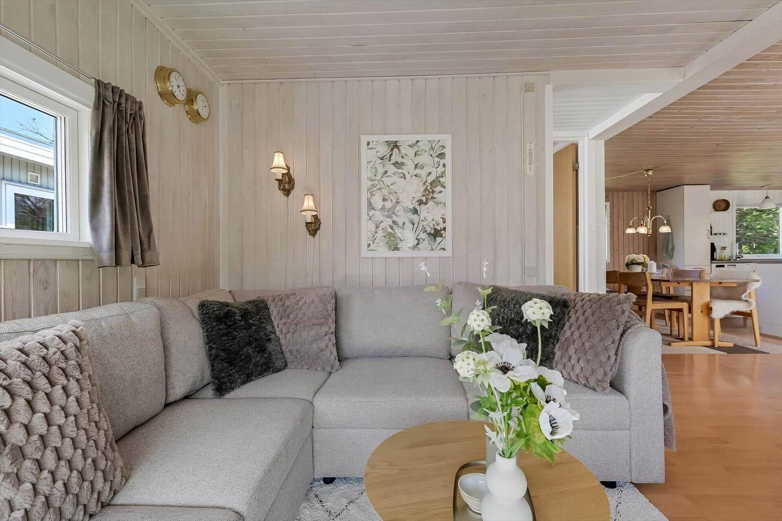Wohnzimmer mit grauem Sofa, Holztisch und Blumen. Küche und Essbereich sind sichtbar.