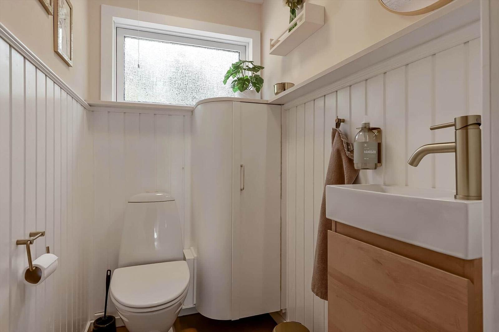 Badezimmer mit Toilette, Waschbecken und Duschabtrennung. Weiße Panele und Holzakzente.