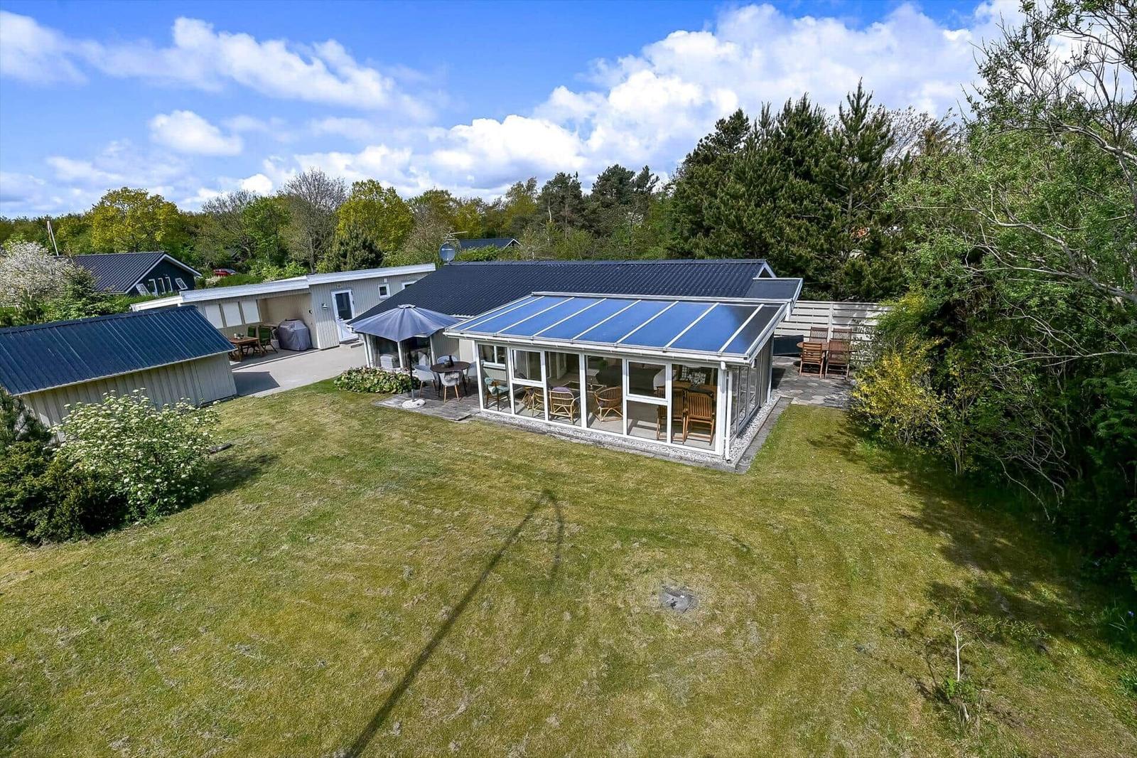 Haus mit Terrasse und Garten. Blauer Sonnenschutz und Holzmöbel sind sichtbar.