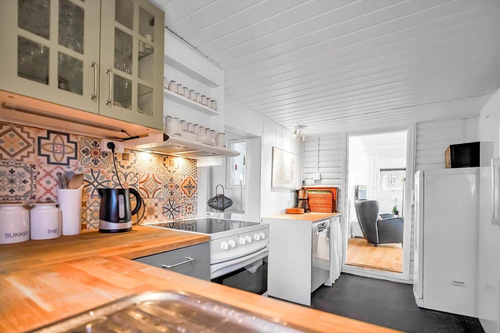 Kitchen with wooden countertop, glass-front cabinet, and colorful tiles on the wall.