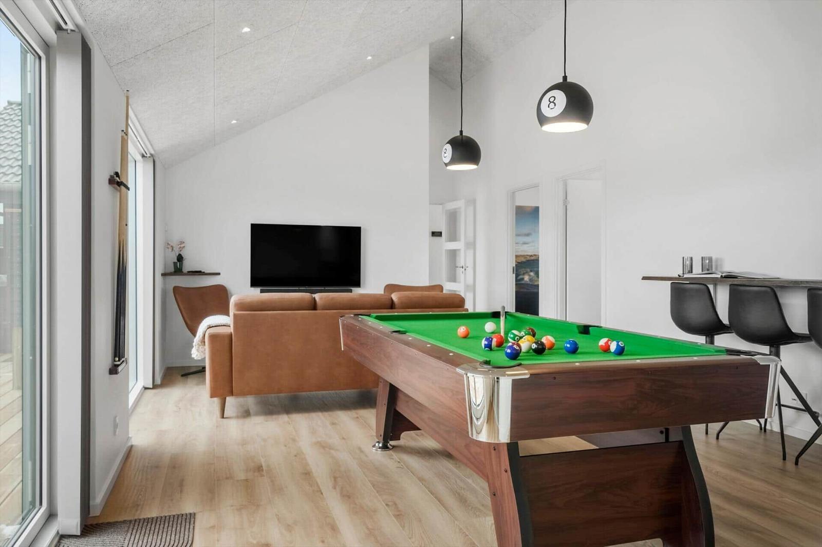 A room with a pool table, sofa, TV, and hanging lamps.