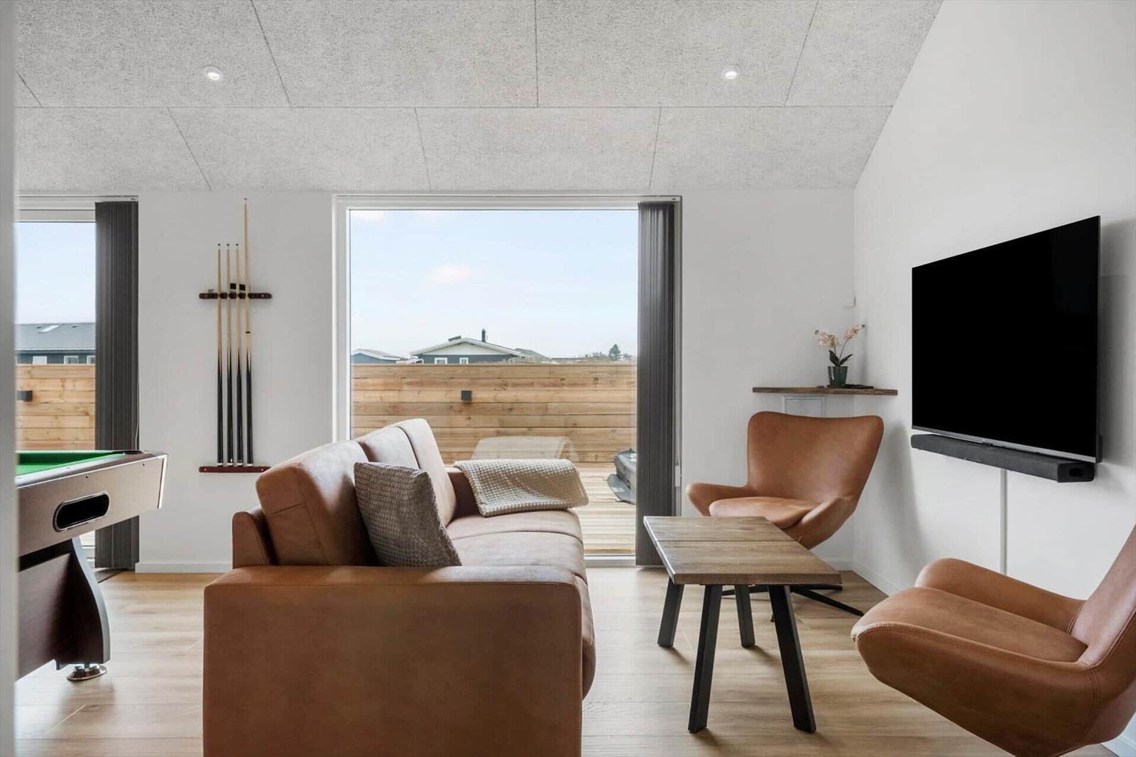 Living room with sofa, chairs, table, and TV. Doorway to terrace with wooden railing.