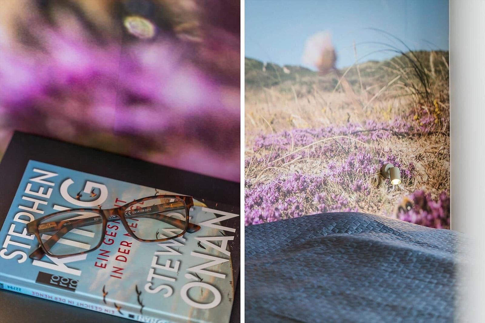A book with glasses rests before a window overlooking a heath landscape.