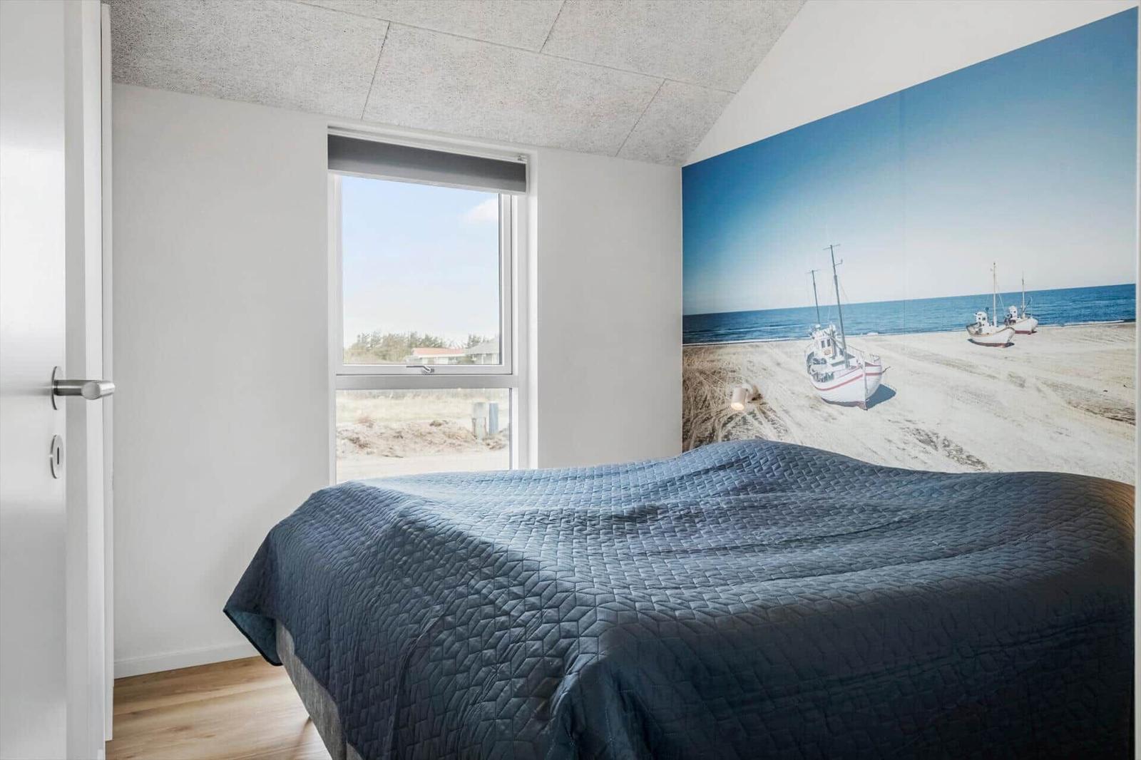 Bedroom with bed, window, and wall mural of boats on beach.