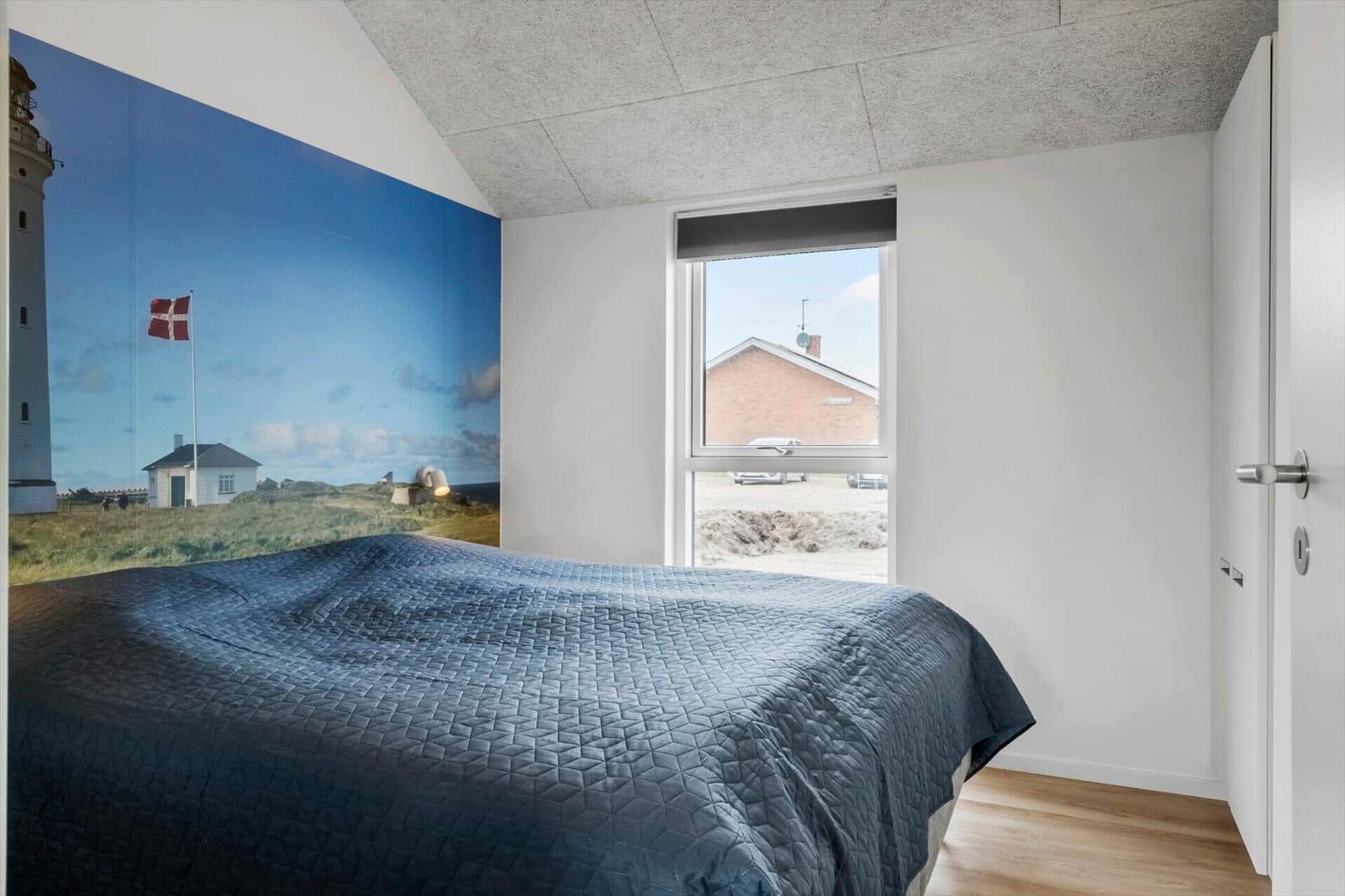 Bedroom with bed, lighthouse mural, and view of a house through window.