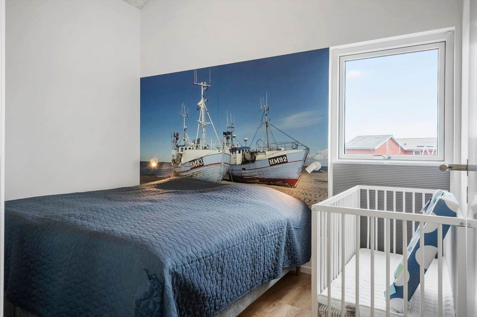 Bedroom with bed, crib, and wall mural of fishing boats.