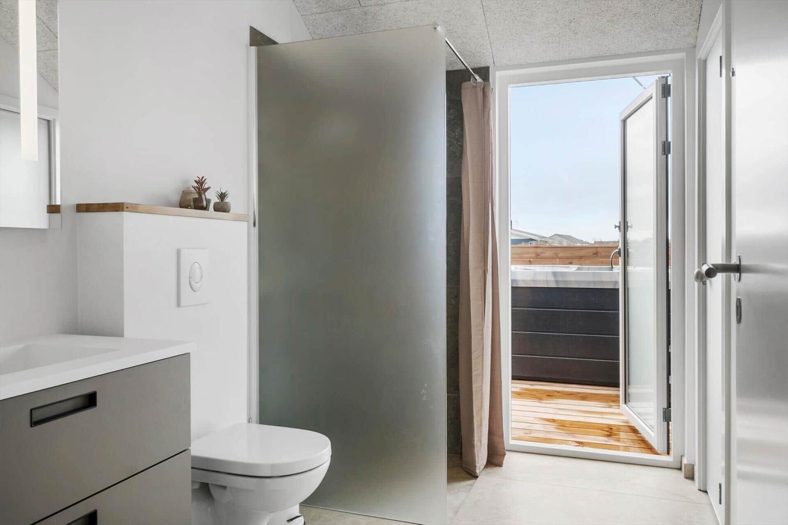 Bathroom with shower, toilet, and view of balcony with hot tub.