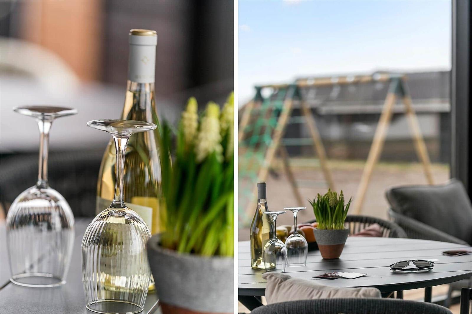 Table with wine glasses, bottle, and plant. Outside view shows balcony seating.