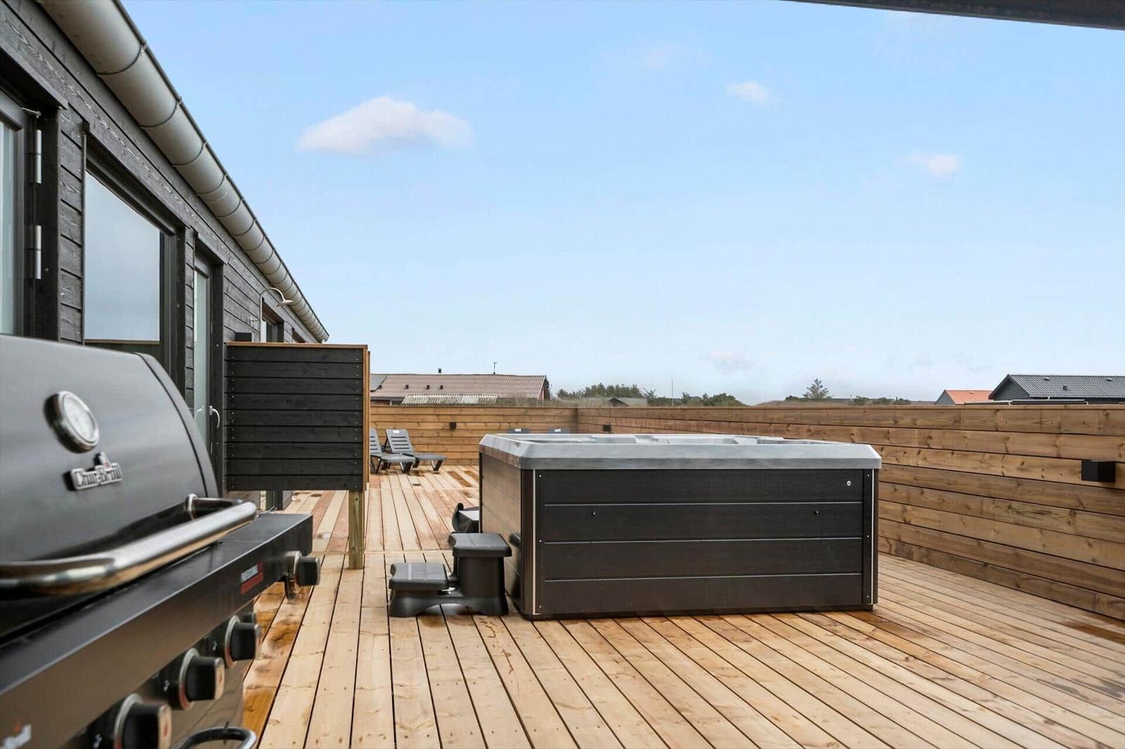 Deck with hot tub, grill, and lounge chairs. Wooden deck and railings.