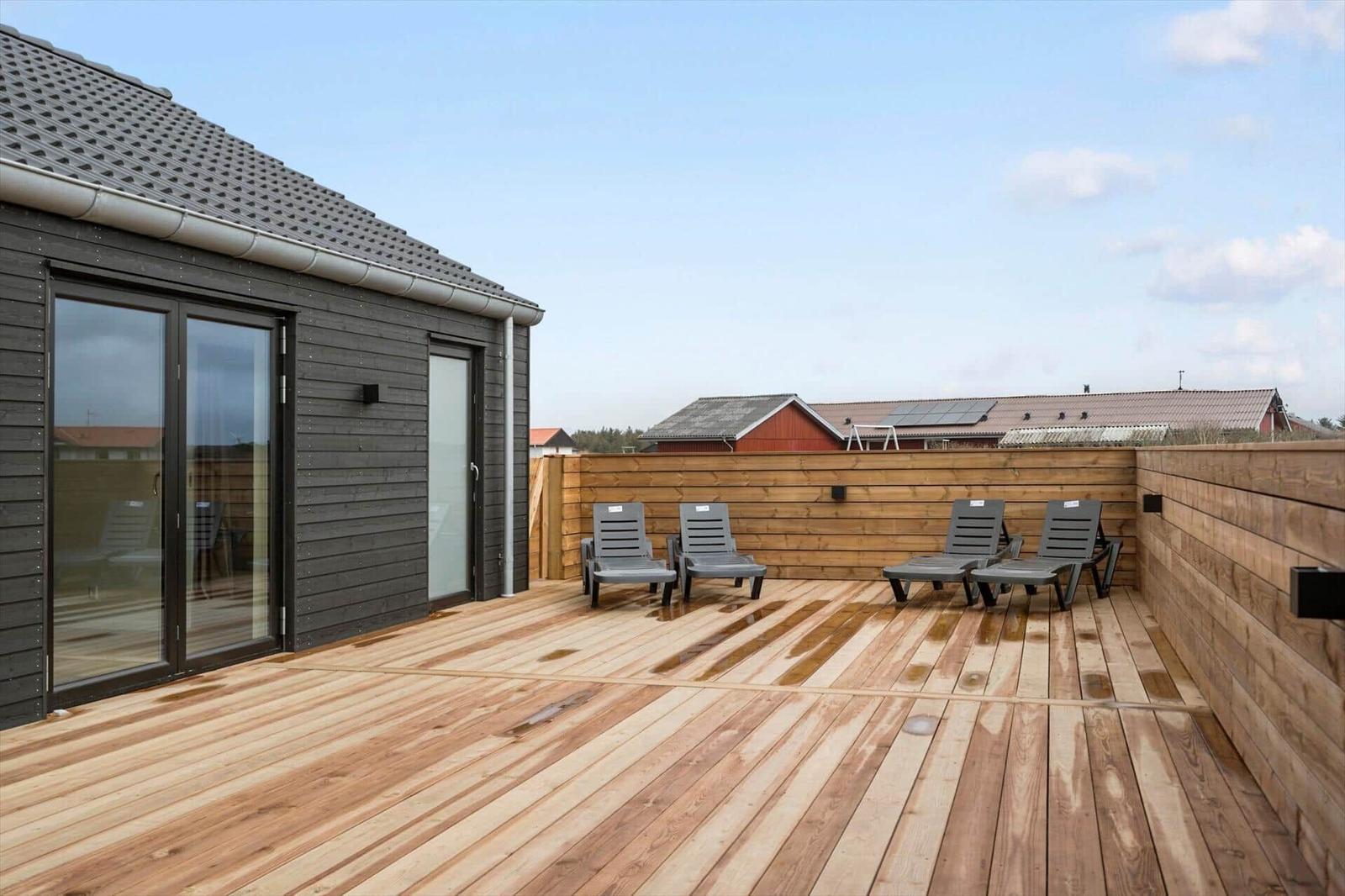 Deck with wooden planks and four lounge chairs next to a house with sliding doors.