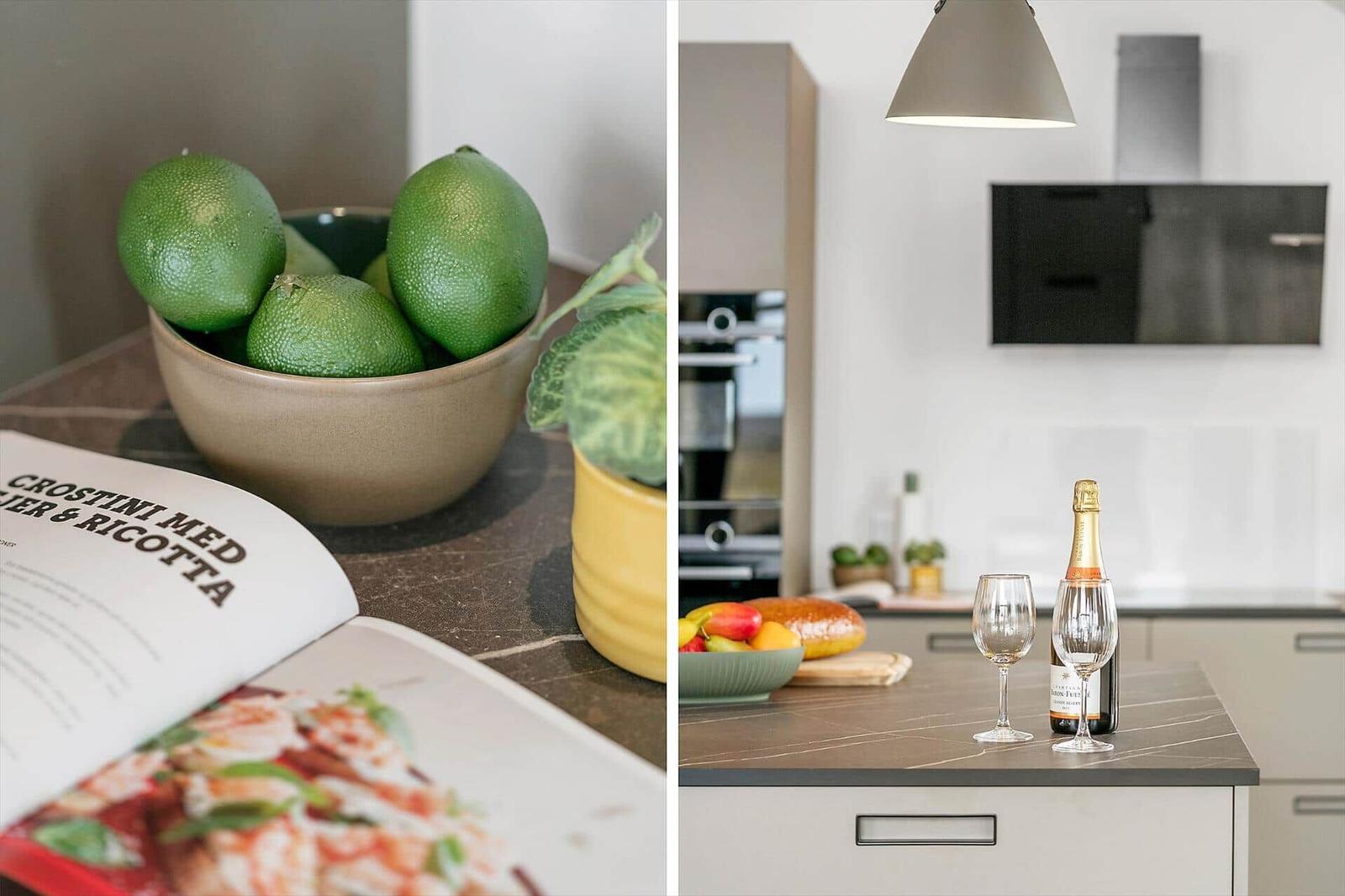 Kitchen area with fruit, wine, and cookbook. Modern setup with light surfaces.