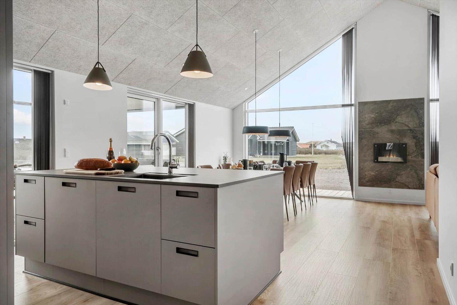Modern kitchen with island, dining area, and fireplace. Large windows with outdoor view.