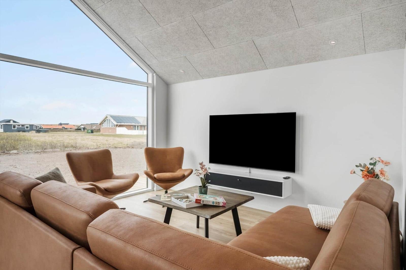 Living room with brown leather furniture, TV, and large window overlooking outdoor area.