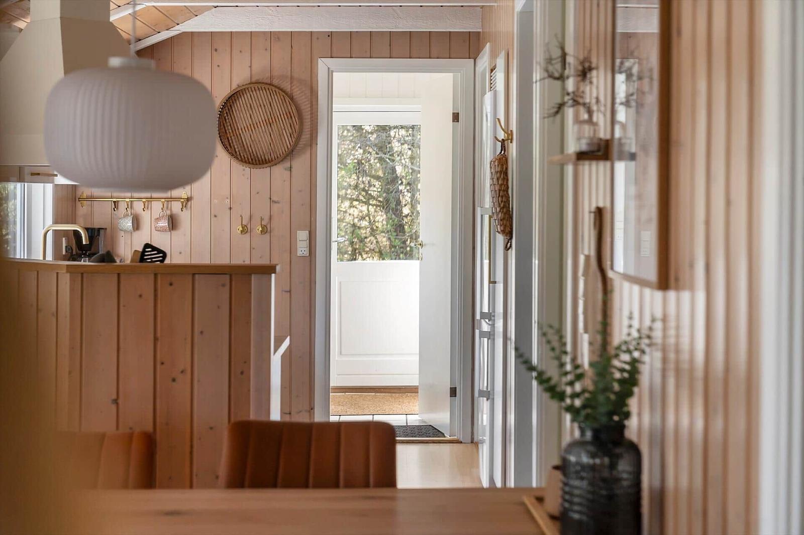 Küche mit Holzwand, Tisch und Stühle. Tür führt nach draußen.
