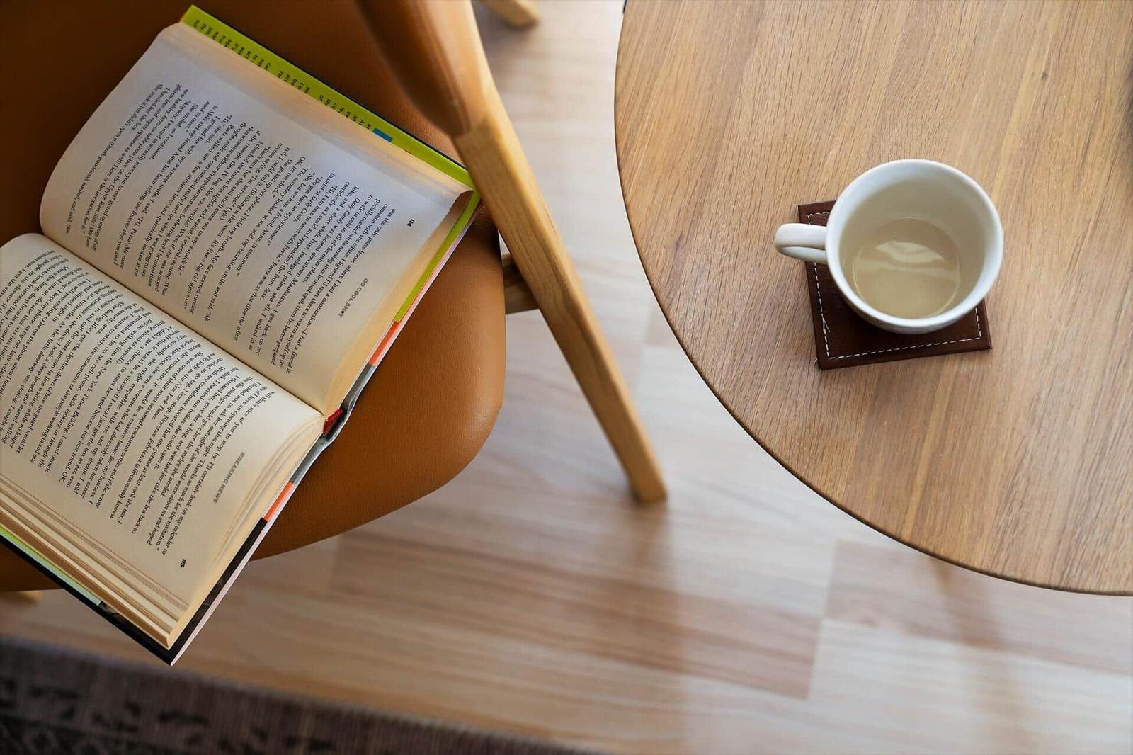 Ein Buch liegt auf einem Stuhl, daneben steht eine Tasse auf einem Tisch.
