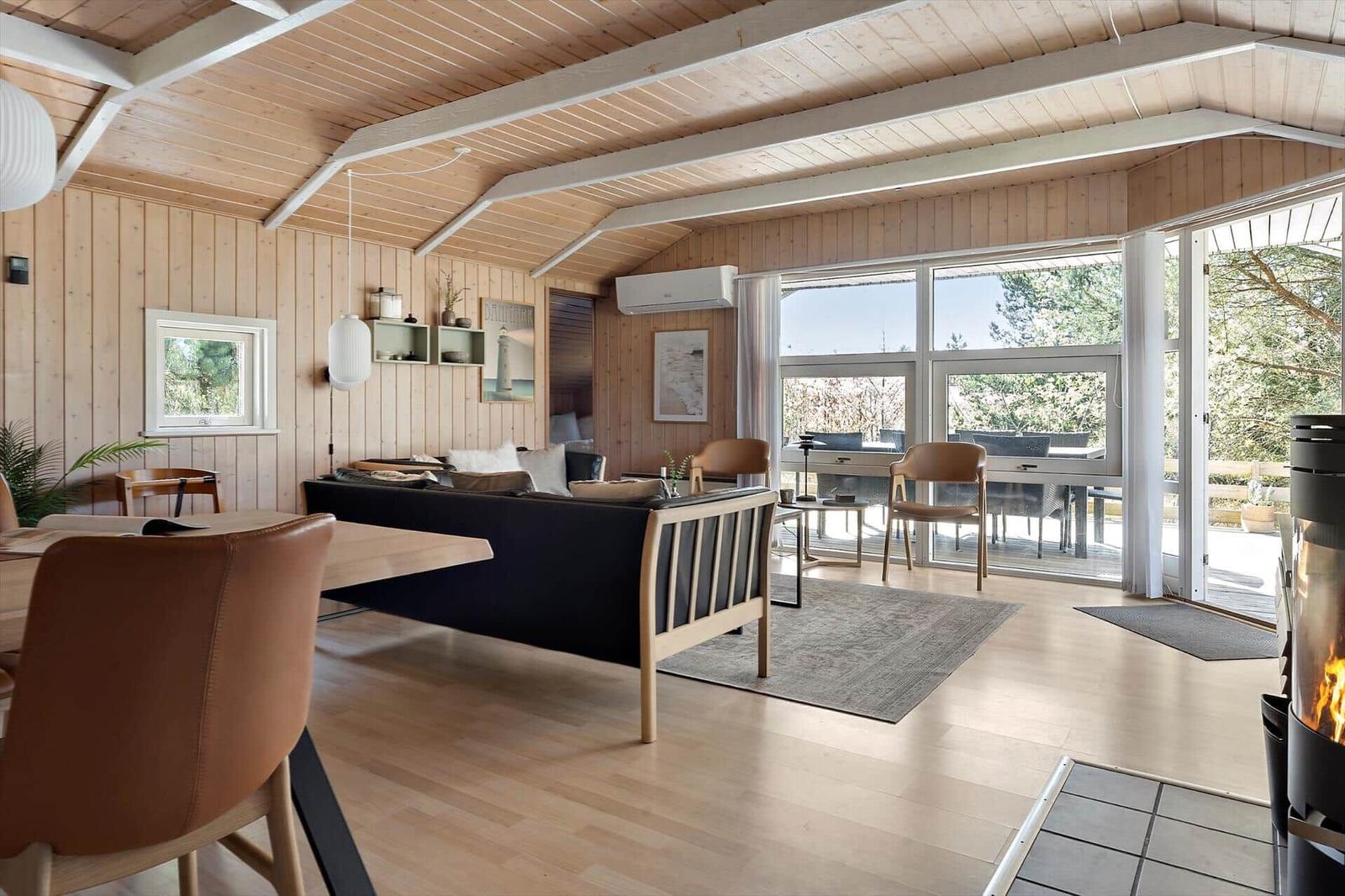 Wohnbereich mit Sofa, Tisch und Stühlen. Holzdecke, Fenster und Kamin sichtbar.