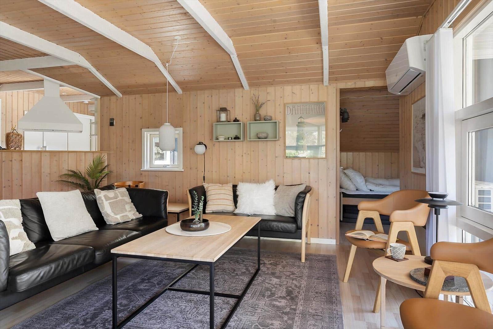 Wohnraum mit Holzwand, Sofa, Tisch und Sessel. Blick in Schlafzimmer.