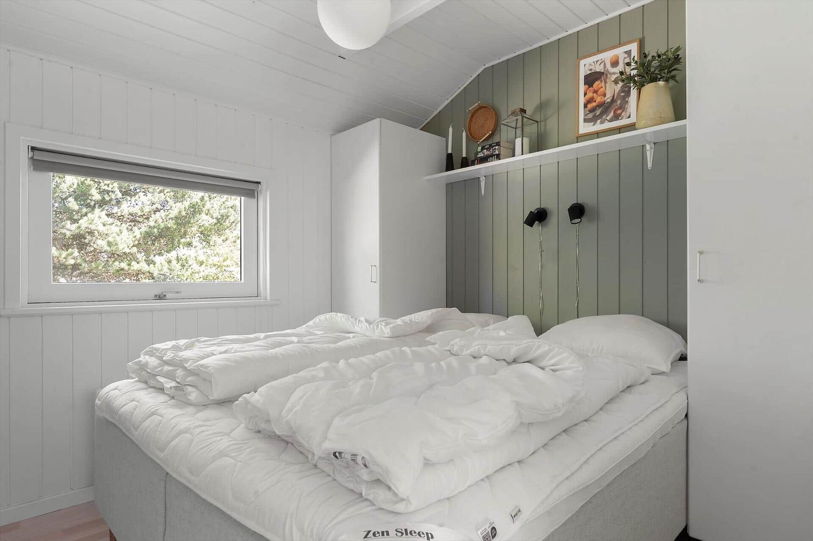 Schlafzimmer mit weißem Bett, Fenster und grünem Paneelwand.