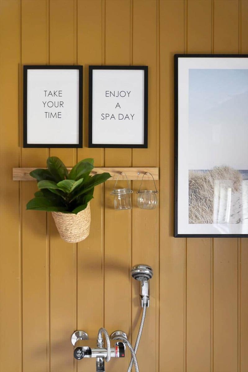 Dusche mit Wandbildern und Pflanze an gelbem Holz