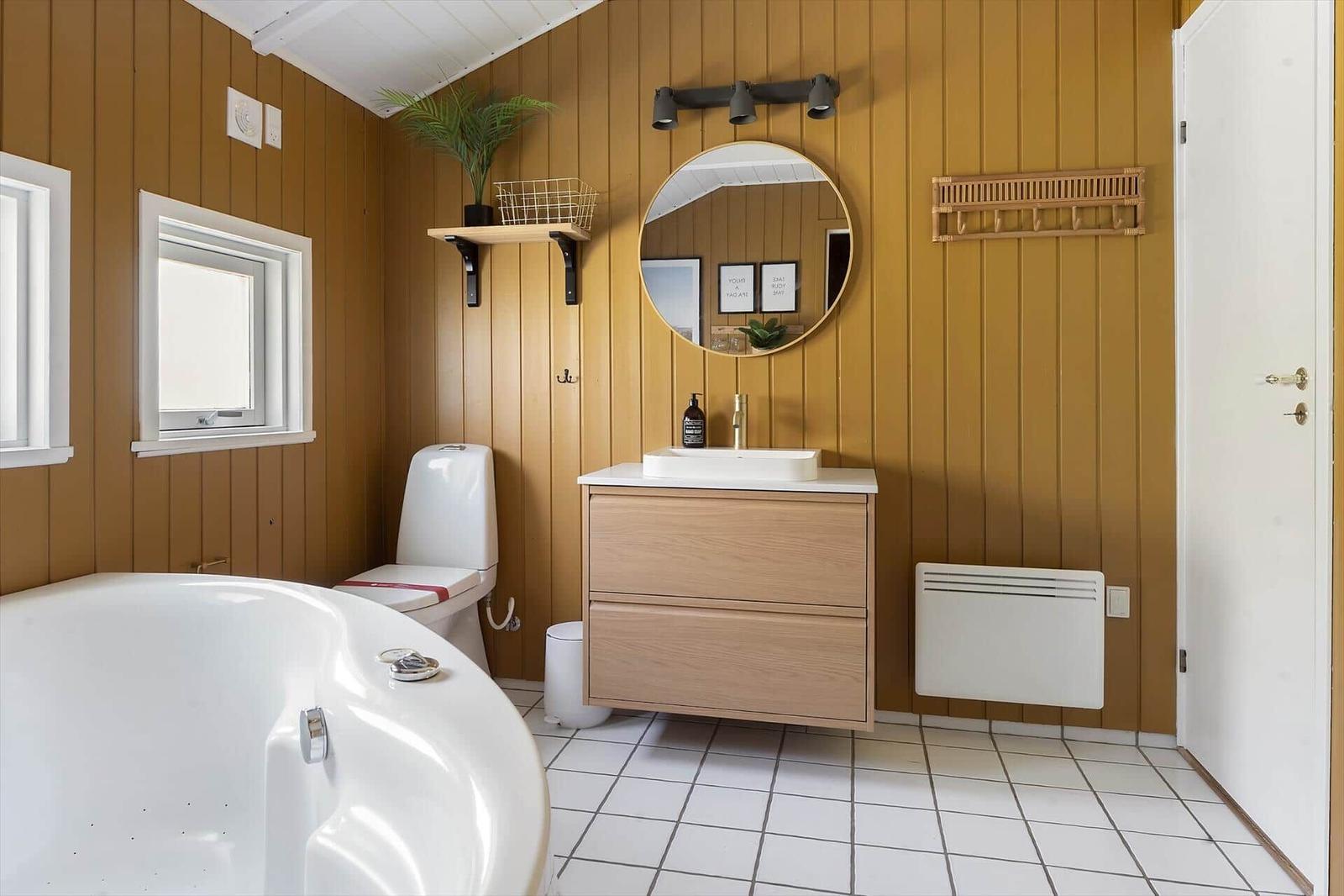 Badezimmer mit Badewanne, Waschtisch und Toilette an Holzwand