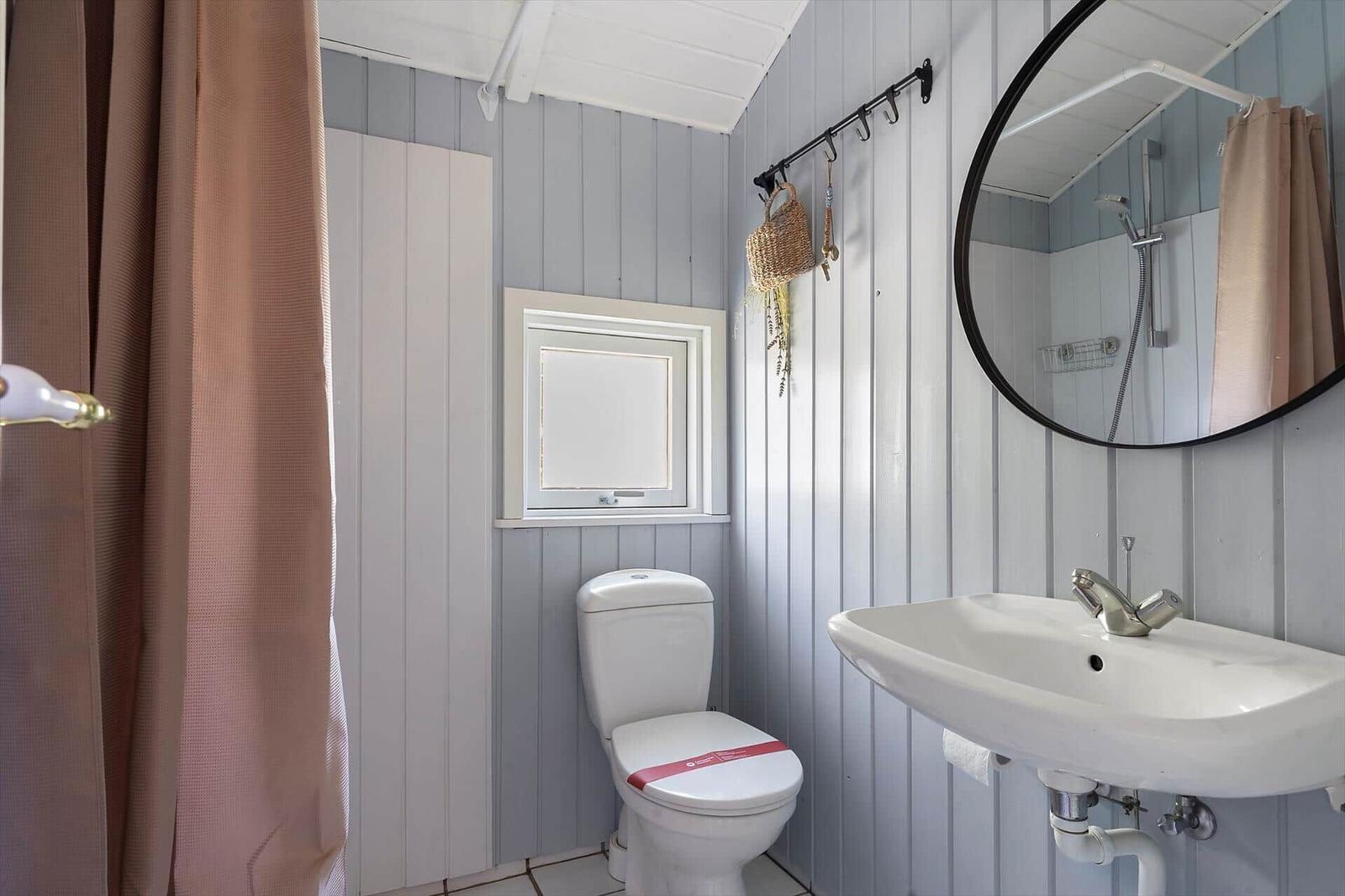 Badezimmer mit Toilette, Waschbecken und Dusche. Holzwände und runder Spiegel.