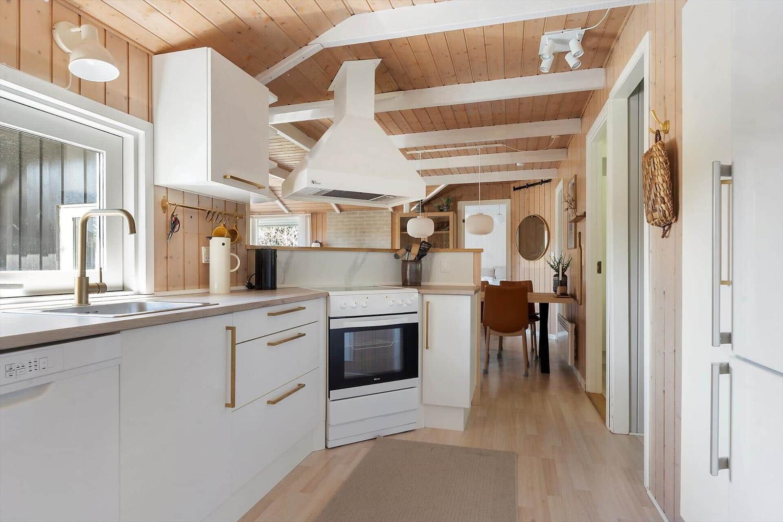 Küche mit weißen Schränken, Holzboden und Holzwand. Esstisch mit brauner Stuhl.