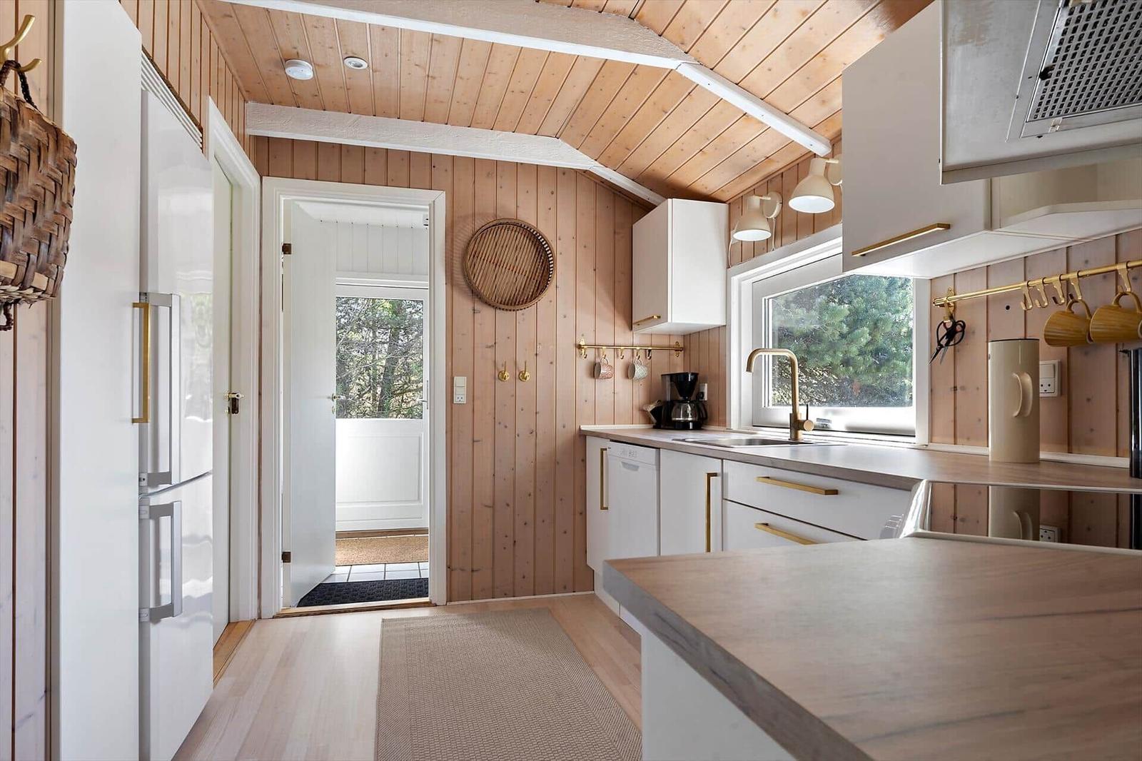 Küche mit Holzwand, weißer Einbauküche und Fenster mit Blick auf Wald.