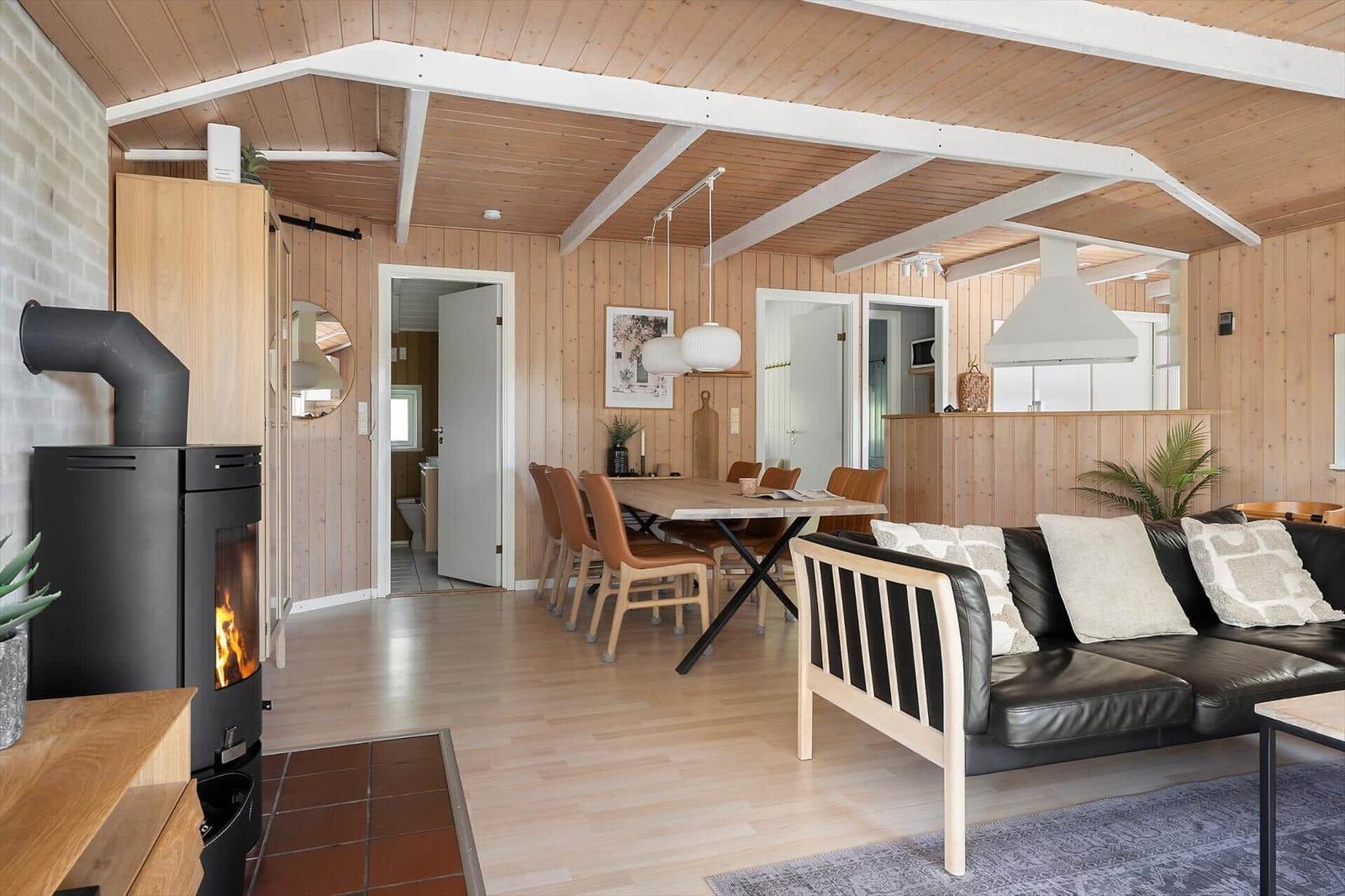 Wohn- und Essbereich mit Holzwand, Kamin und Sofa.