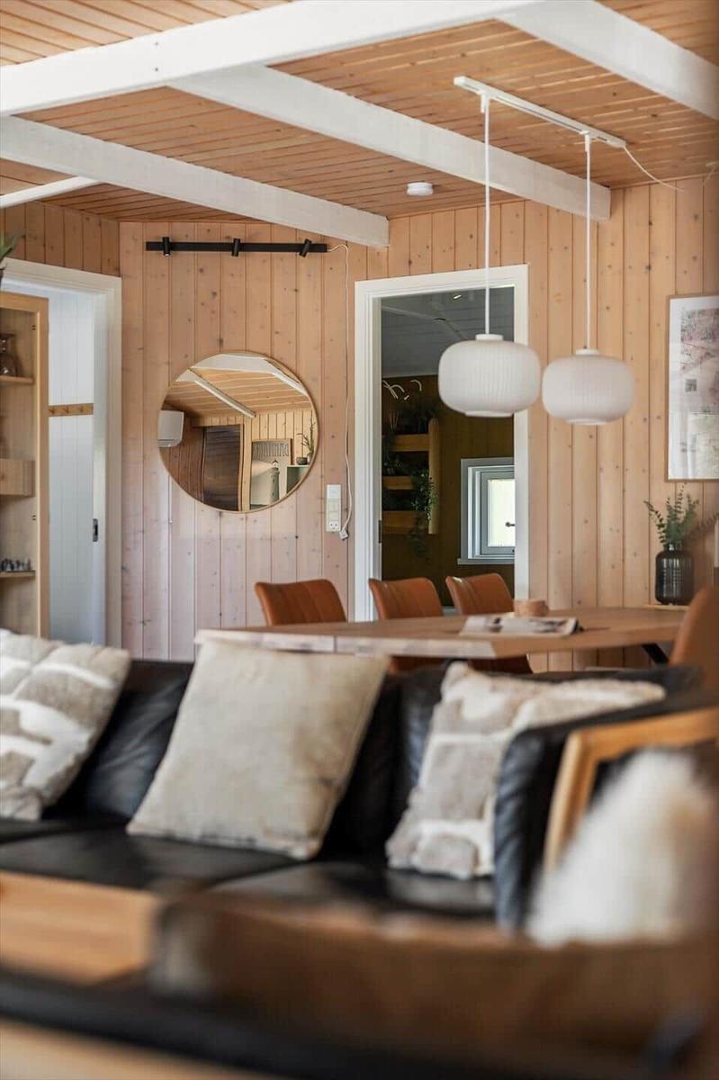 Wohn- und Essbereich mit Holzwand und Decke, schwarzer Couch und runden Lampen.