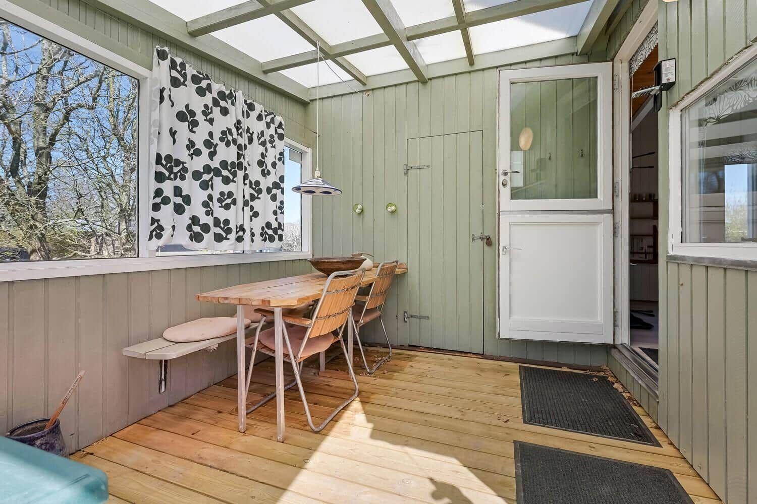 Terrasse mit Tisch, Stühlen und Fenstern. Holzboden und grüne Wände.