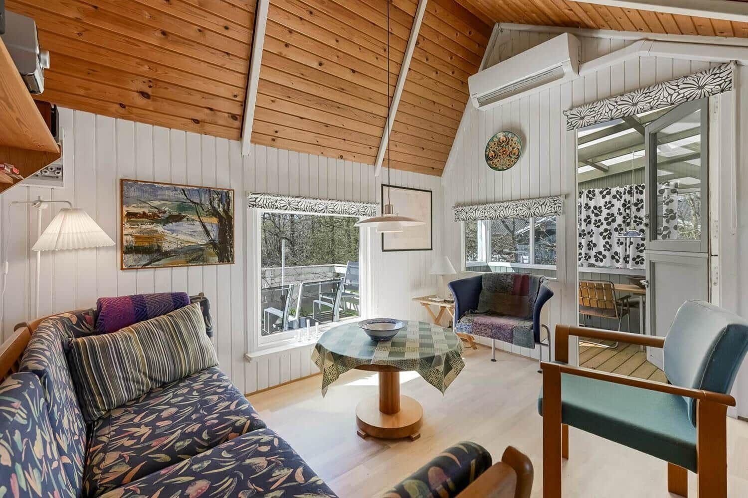 Wohnzimmer mit Sofa, Tisch und Stühlen. Holzdecke und Fenster mit Blick.