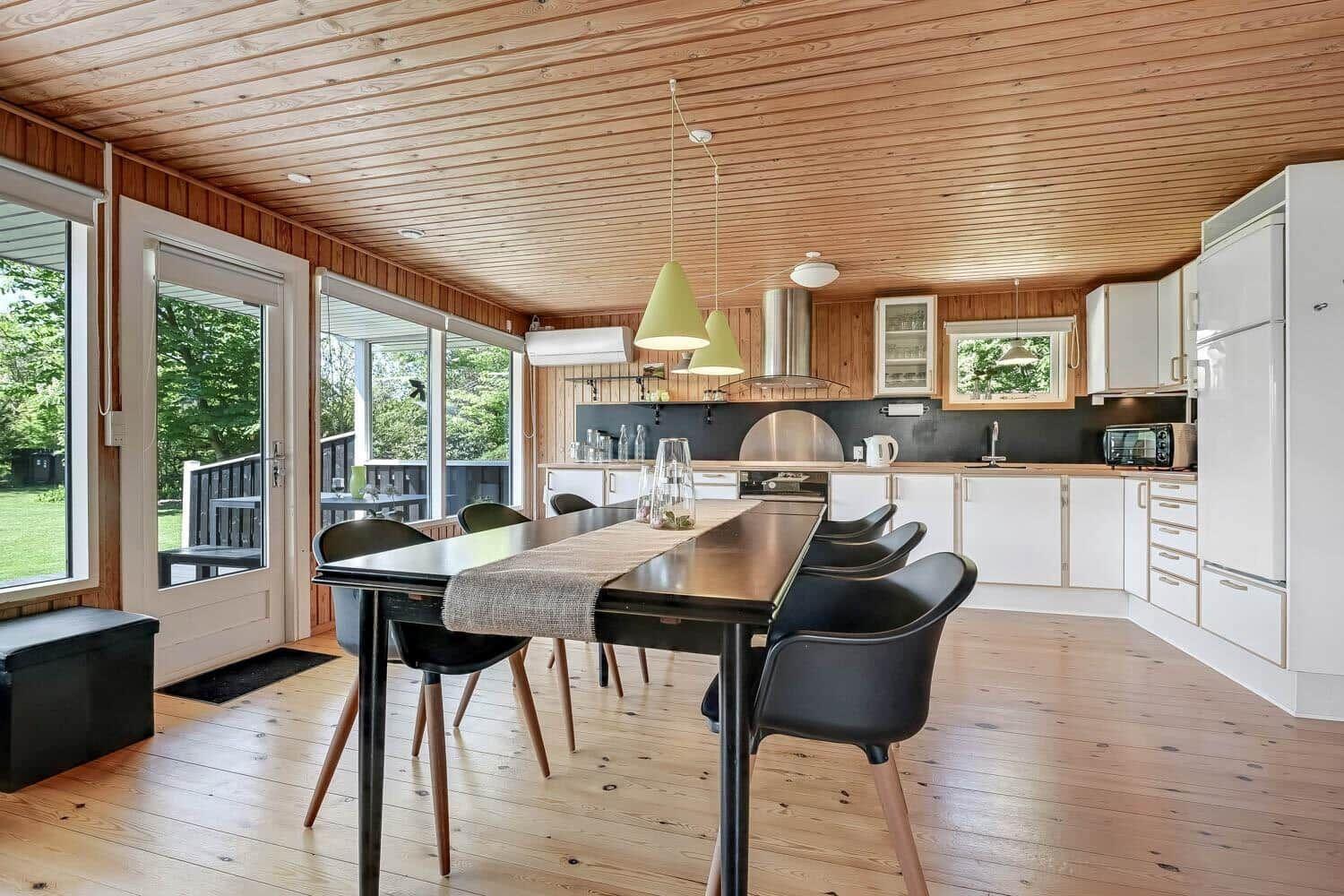Kitchen and dining area with wooden floor and ceiling, white cabinetry, and large table with chairs.