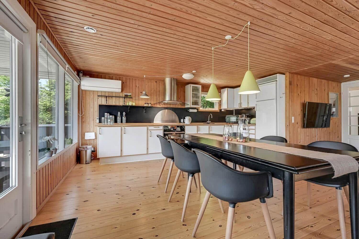 Kitchen with dining area, wooden ceiling and floor, white cabinets, black countertop, and dining table with chairs.