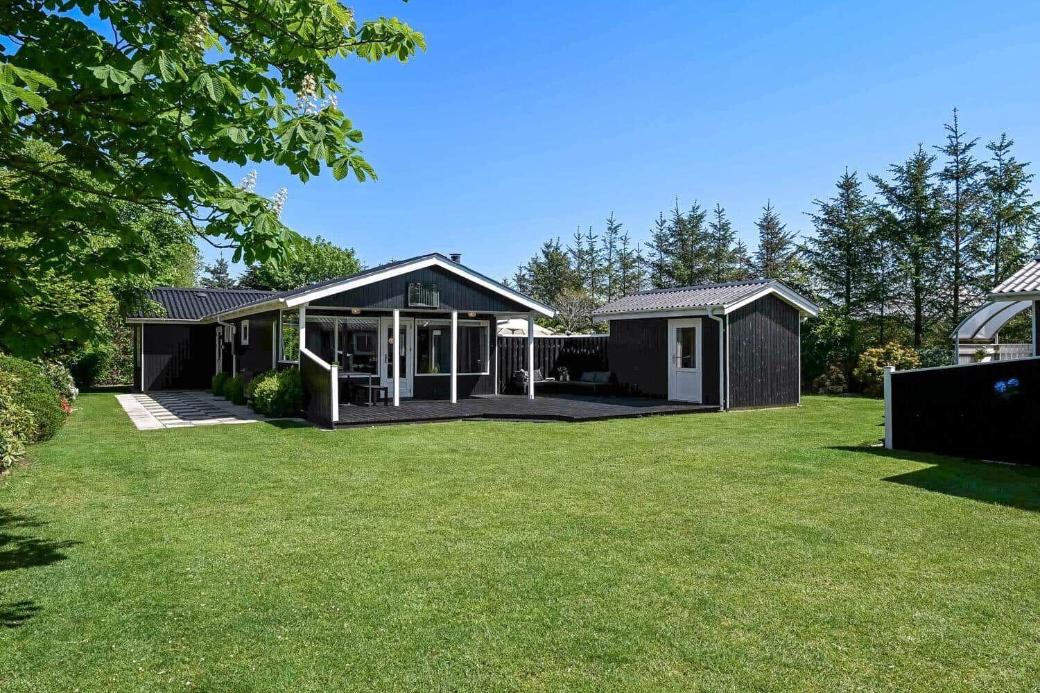 Black wooden house with terrace and green lawn under blue sky.