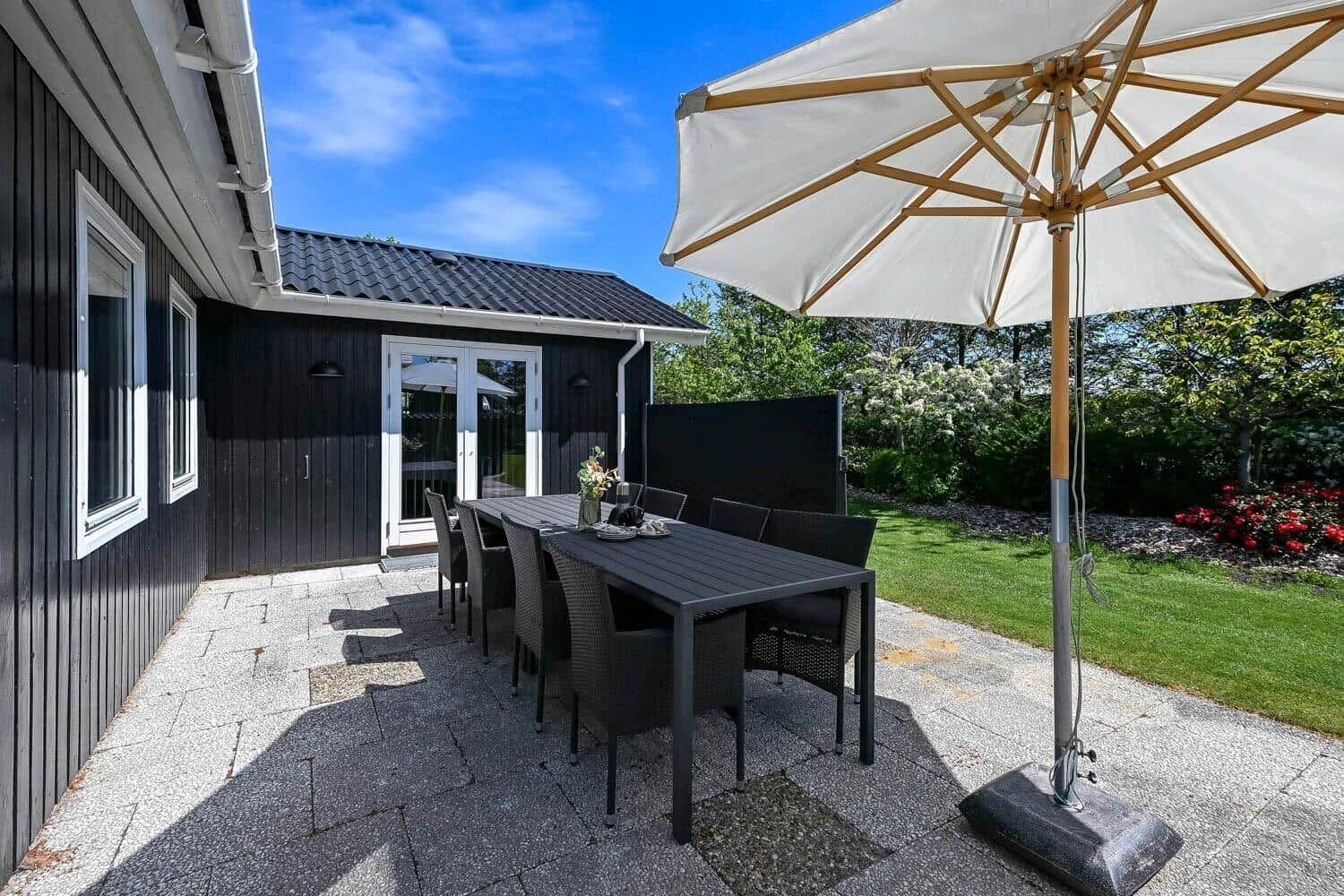 Terrace with table, chairs, and umbrella. Background: garden and house.