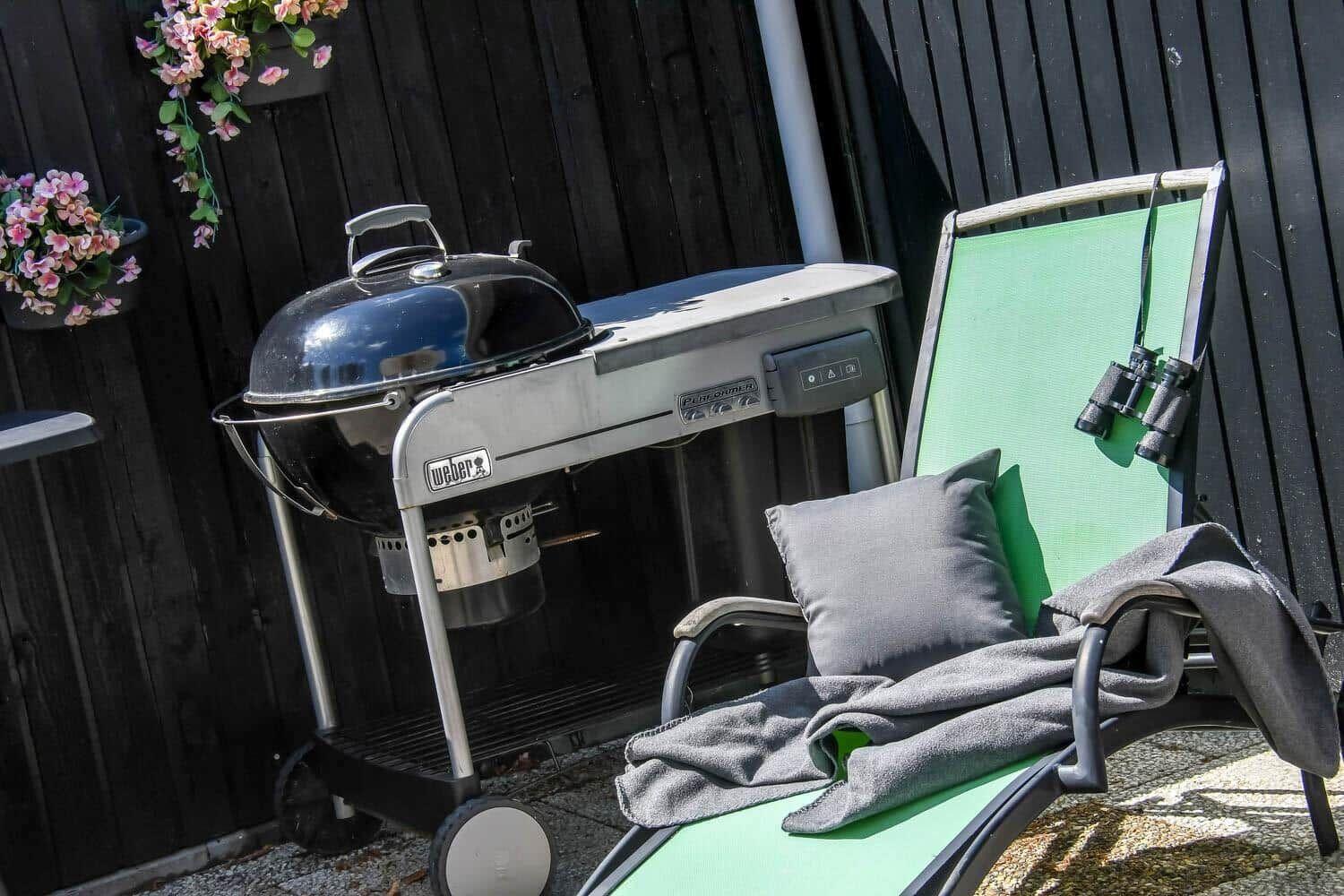 Grill and lounge chair with pillow and blanket in the garden.