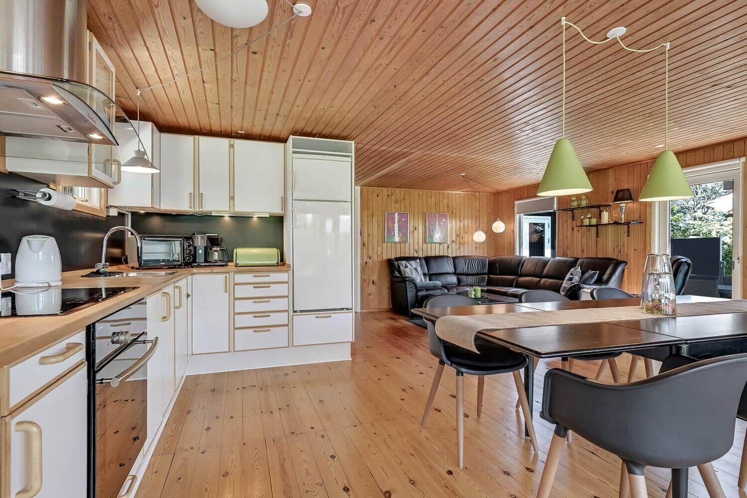 Kitchen with dining area and living room under wooden ceiling.