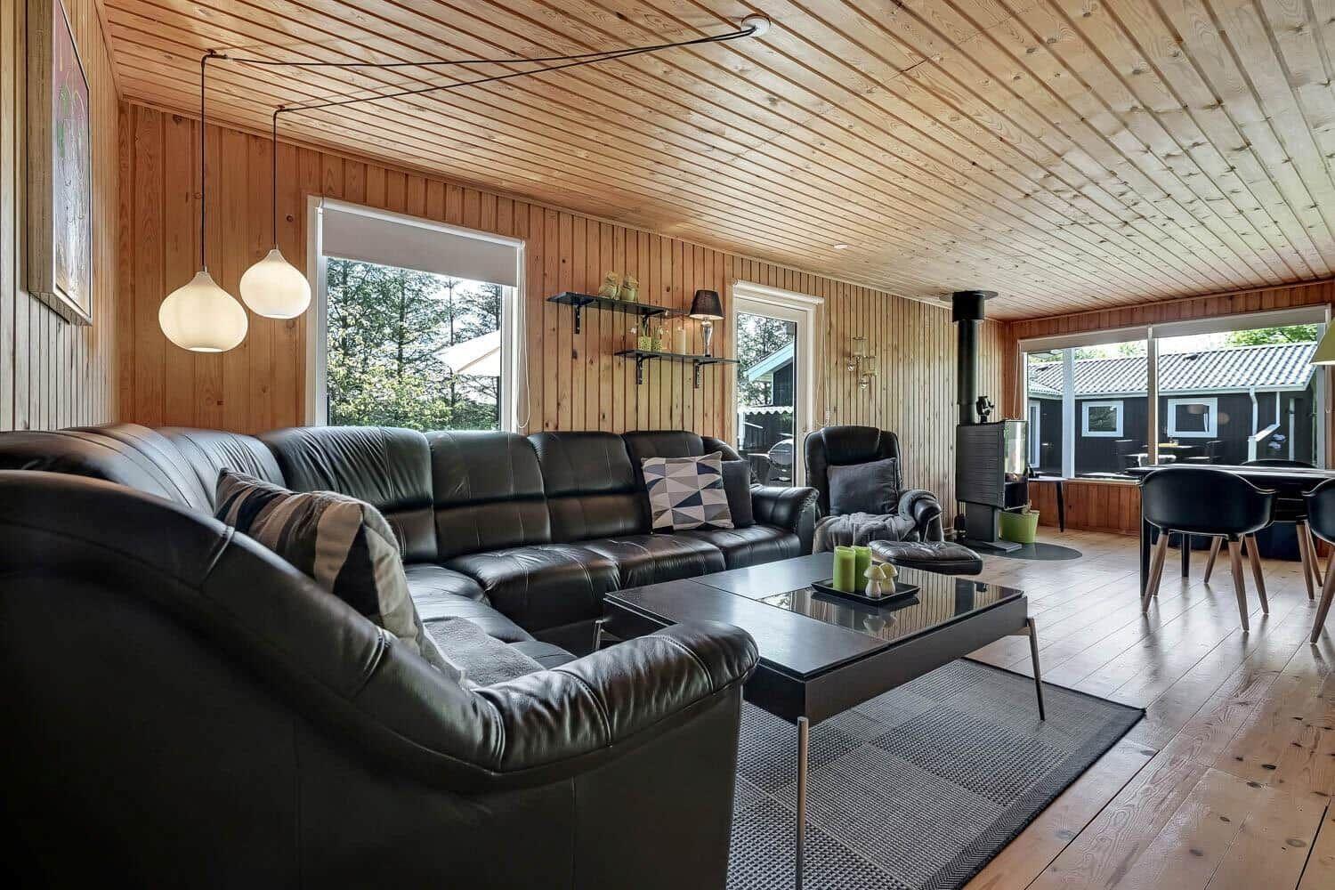 Living room with leather sofa, glass table, and wood walls. Access to kitchen.