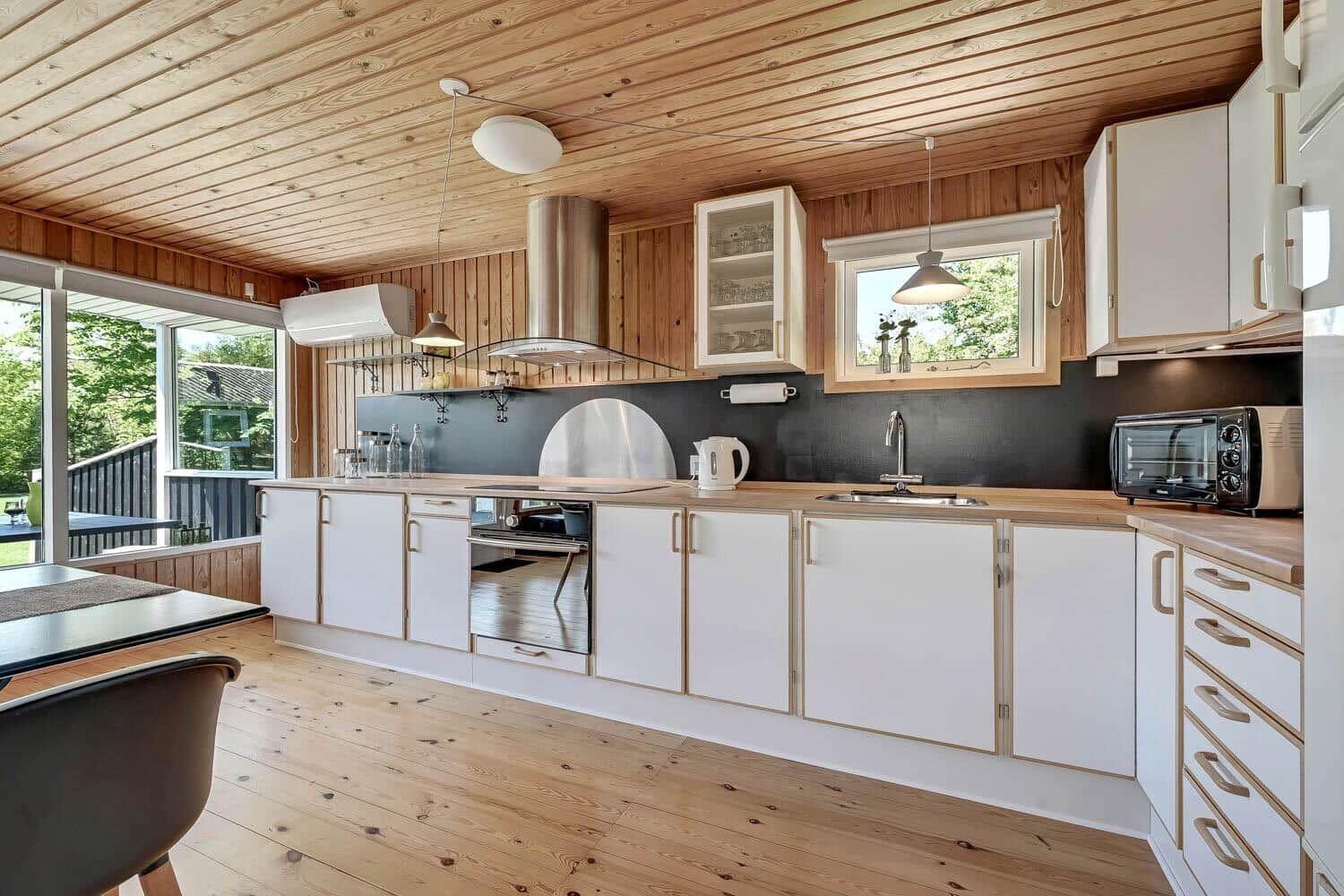 Modern kitchen with wooden ceiling, white cabinets, and built-in stove.