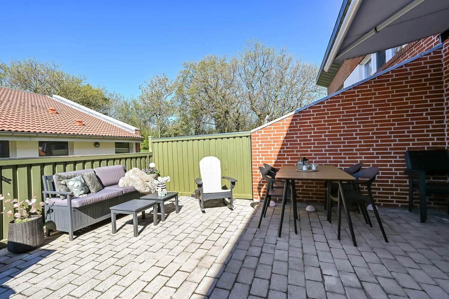 Terrace with seating group, table and chairs, red brick wall and green fence.