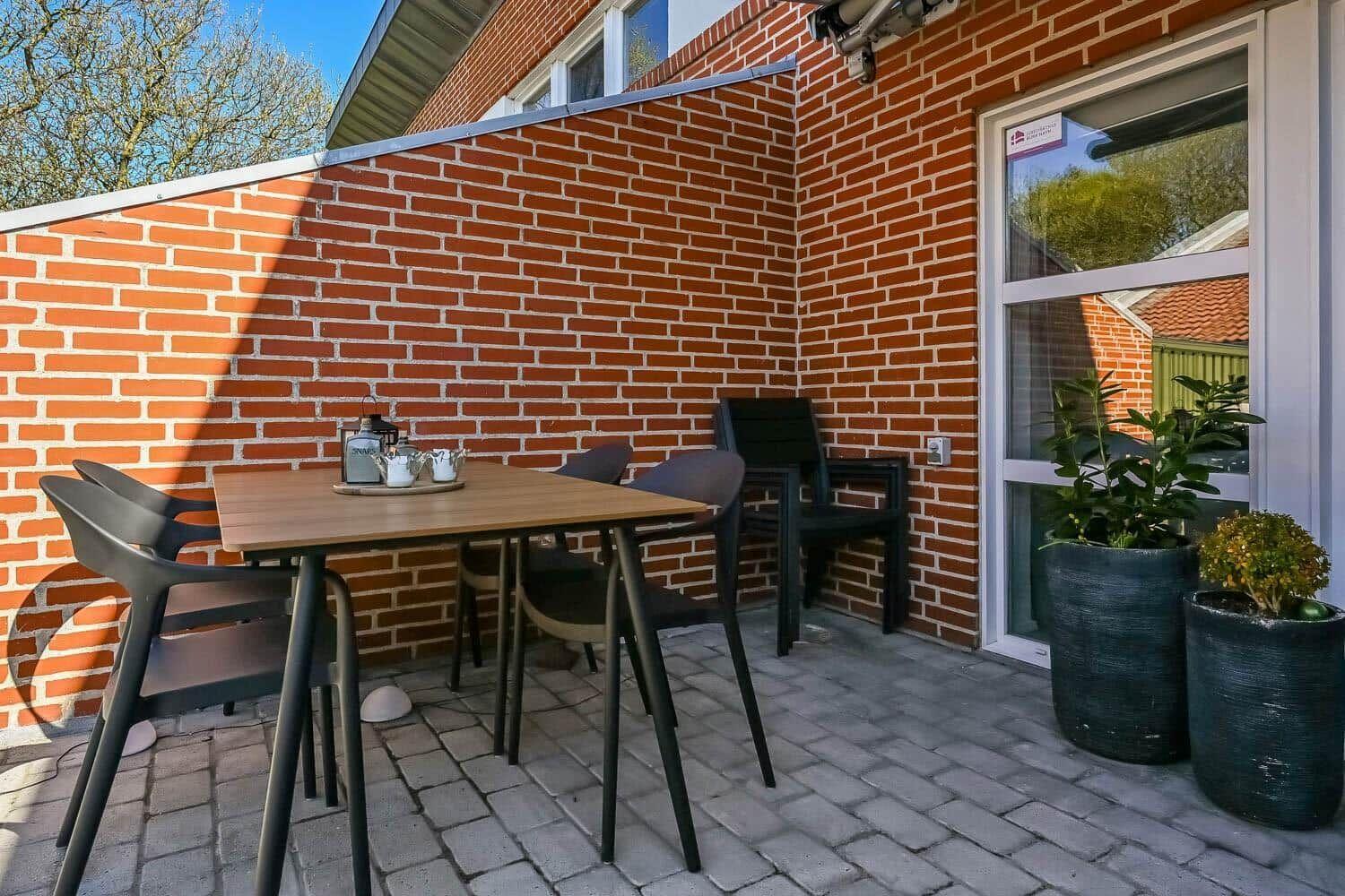 Terrace with table, chairs, and plants against red brick wall.