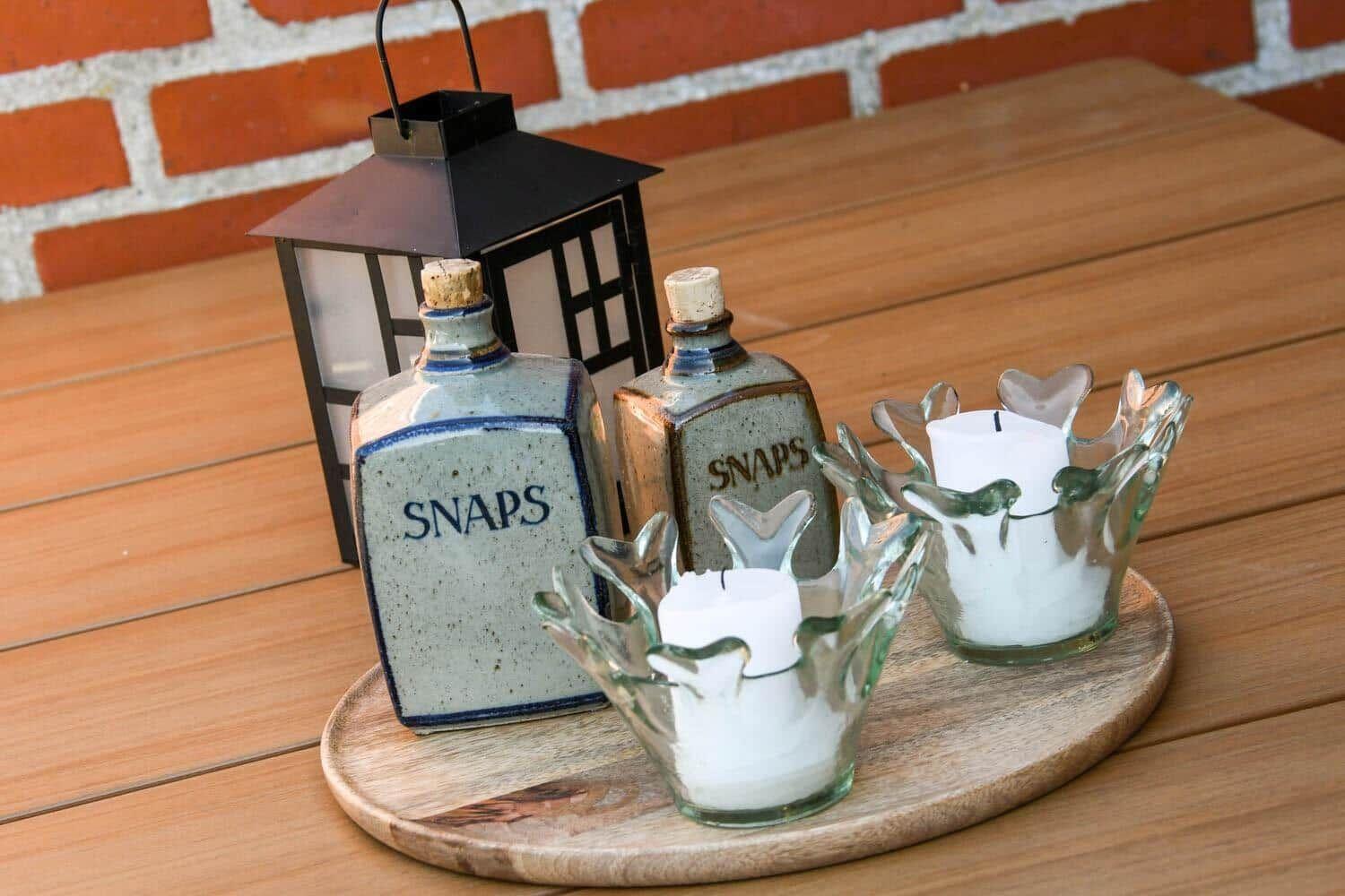 Wooden tray with candle holders, bottles, and lantern on terrace.
