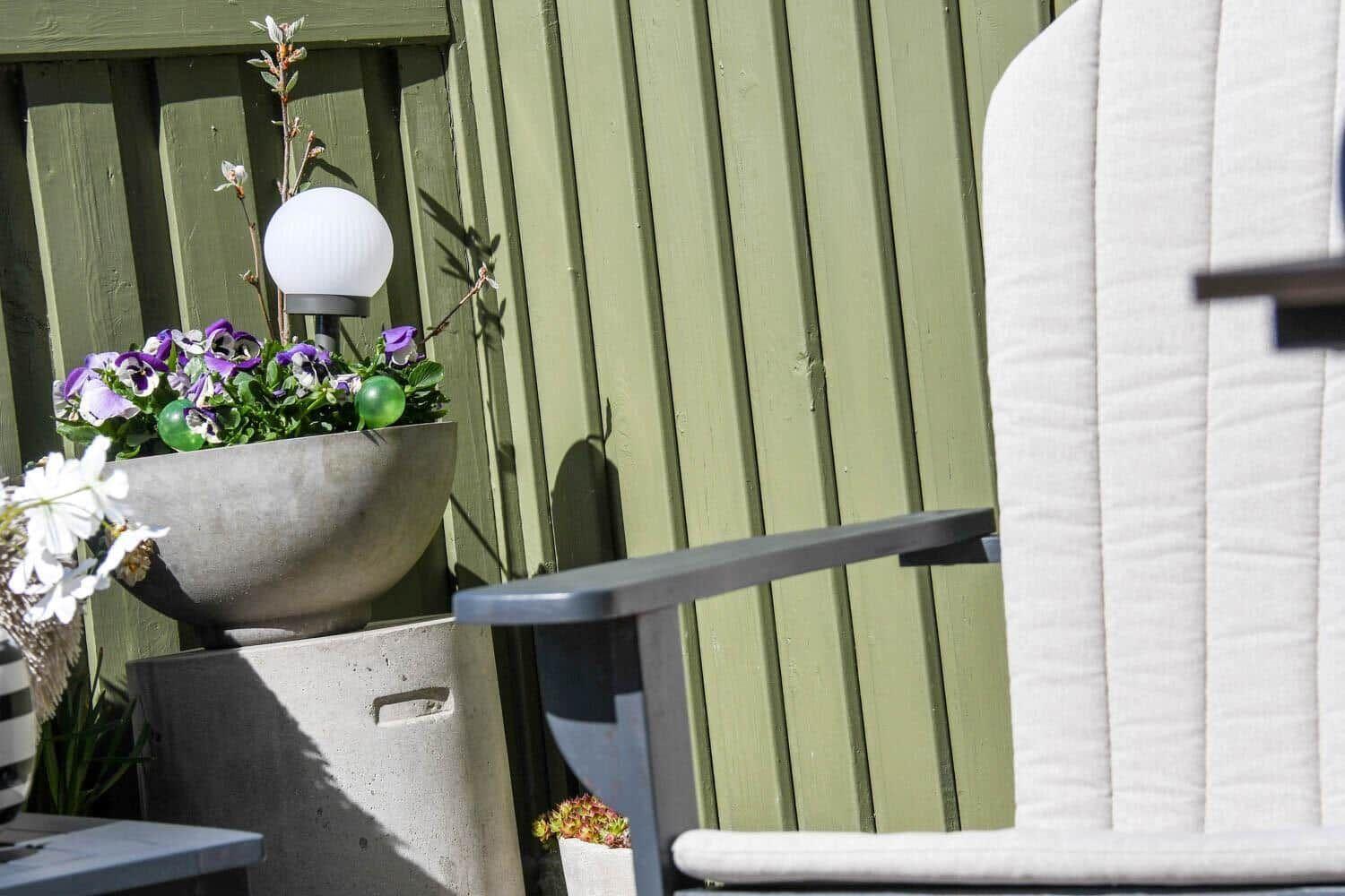 Outdoor area with chair, plants, and lighting against green wooden fence.
