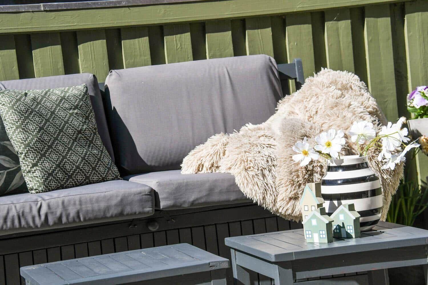 Terrace sofa with cushions and fur blanket. Table with vases and house models.