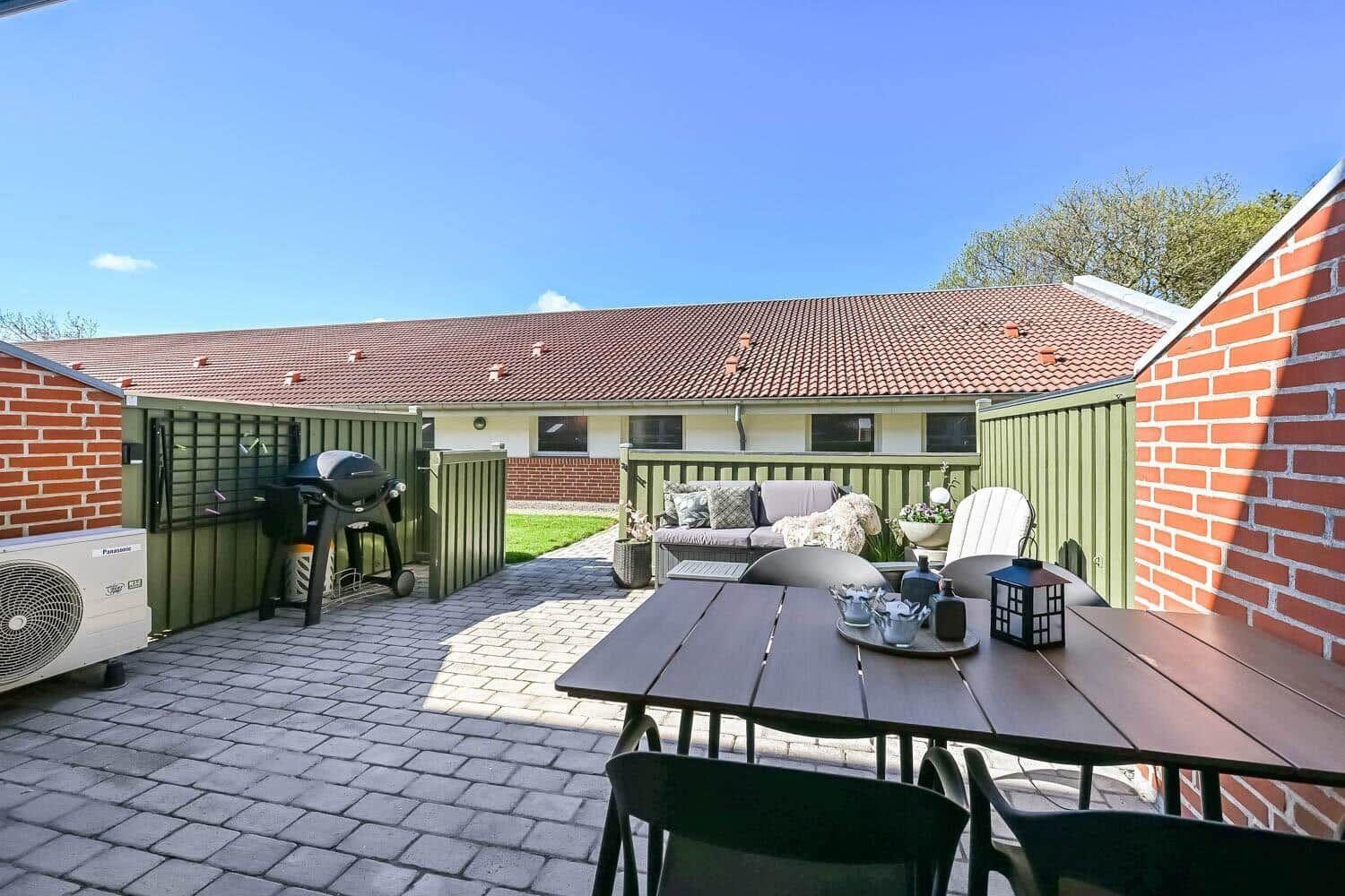 Terrace with table, chairs, sofa, and grill. Backyard with garden and house.