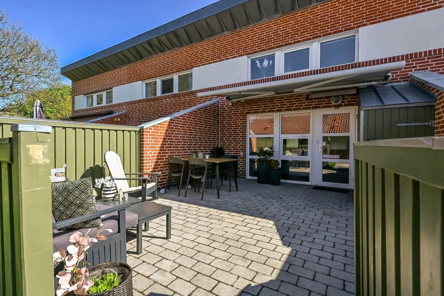 Terrace with seating and table. Background: red brick wall and entrance door.